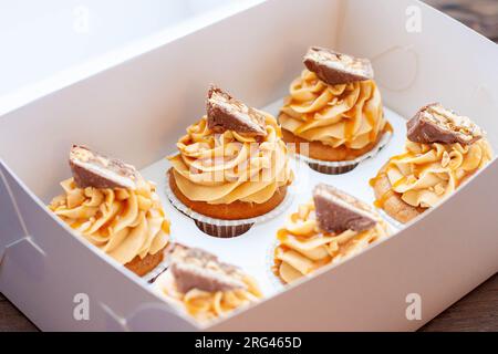 Magnifiques cupcakes au beurre de cacahuète, caramel salé et barre de chocolat sur boîte cadeau en carton Banque D'Images