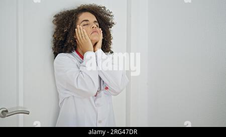 Jeune belle femme hispanique médecin appuyé sur la porte stressé à la clinique Banque D'Images