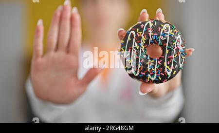 Jeune femme blonde diététicienne tenant un beignet faisant un geste d'arrêt avec la main à la clinique Banque D'Images