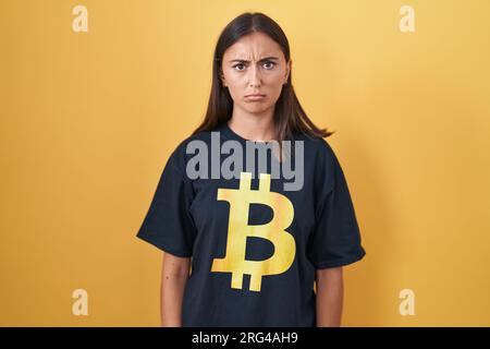 Jeune femme hispanique portant un t-shirt bitcoin sceptique et nerveuse, fronçant les sourcils bouleversée à cause du problème. personne négative. Banque D'Images