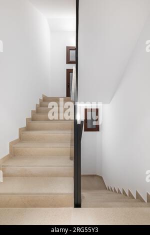 Photo verticale d'un escalier confortable propre avec passerelle beige balustrades en métal noir et murs blancs dans un hôtel dans une nouvelle zone urbaine confortable. CopySpace Banque D'Images