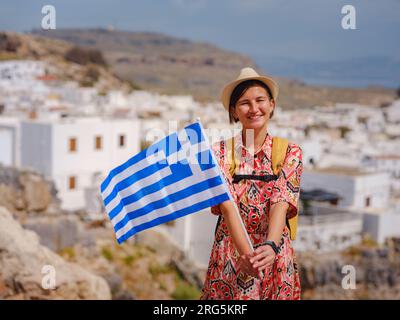 Jeune femme voyageant avec drapeau grec national profitant de la vue de Lindos. Voyage en Grèce, îles méditerranéennes en dehors de la saison touristique. Banque D'Images