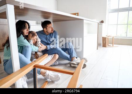 Famille effrayée se cachant sous la table à manger pendant le tremblement de terre dans la cuisine Banque D'Images