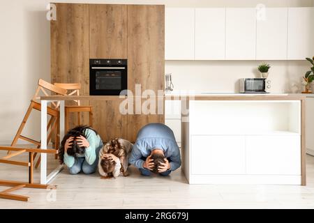 Famille effrayée se cachant sous la table à manger pendant le tremblement de terre dans la cuisine Banque D'Images