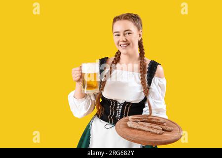 Jeune femme dans des vêtements traditionnels allemands avec de la bière et des saucisses sur fond jaune Banque D'Images