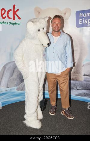 Hambourg, Allemagne. 07 août 2023. Sasha, chanteuse, se tient à côté d'une personne en costume d'ours polaire devant un mur de presse au zoo de Hagenbeck après le baptême de l'ours polaire. La chanteuse baptisa le bébé ours polaire, né le 19 décembre 2022, sous le nom d'Anouk. Crédit : Georg Wendt/dpa/Alamy Live News Banque D'Images