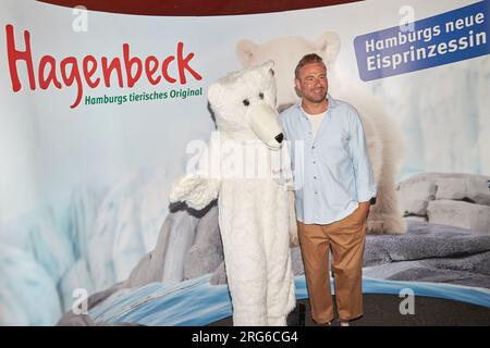 Hambourg, Allemagne. 07 août 2023. Sasha, chanteuse, se tient à côté d'une personne en costume d'ours polaire devant un mur de presse au zoo de Hagenbeck après le baptême de l'ours polaire. La chanteuse baptisa le bébé ours polaire, né le 19 décembre 2022, sous le nom d'Anouk. Crédit : Georg Wendt/dpa/Alamy Live News Banque D'Images