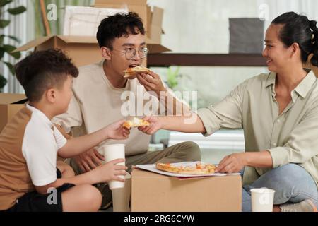 Famille fatiguée et affamée mangeant de la pizza fraîche après avoir emballé des affaires dans des boîtes Banque D'Images