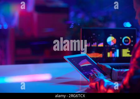 Vu de derrière femme d'affaires moderne avec ordinateur portable travaillant avec des graphiques et en utilisant un tablet PC dans le bureau moderne. Banque D'Images