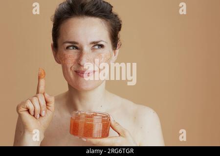 pensive moderne femme de 40 ans avec gommage du visage isolé sur beige. Banque D'Images