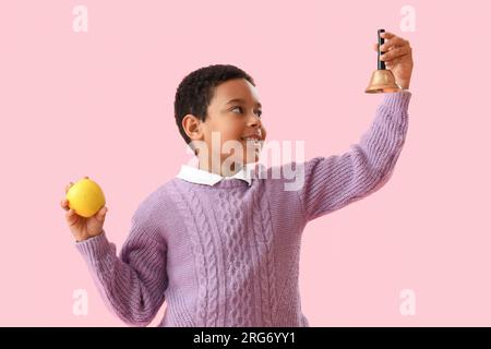 Petit écolier afro-américain avec cloche et pomme sur fond rose Banque D'Images