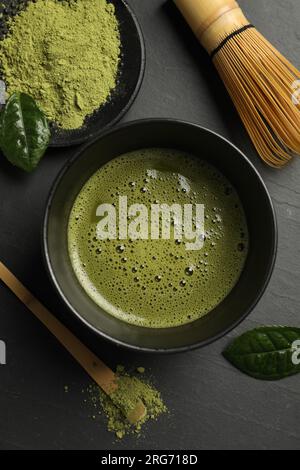 Tasse de thé matcha frais, fouet en bambou, cuillère et poudre verte sur table noire, mise à plat Banque D'Images