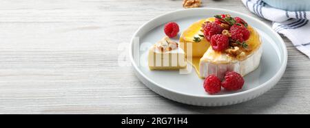 Savoureux fromage brie avec des framboises, des noix et du miel sur une table en bois blanc, espace pour le texte. Conception de bannière Banque D'Images