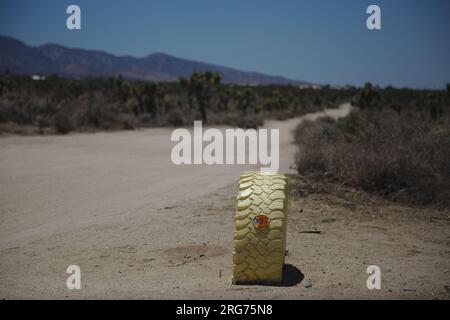 Pneu vertical en sable peint en jaune avec un réflecteur orange. Le pneu est partiellement enterré dans le sable sur le côté d'un chemin de terre. Banque D'Images