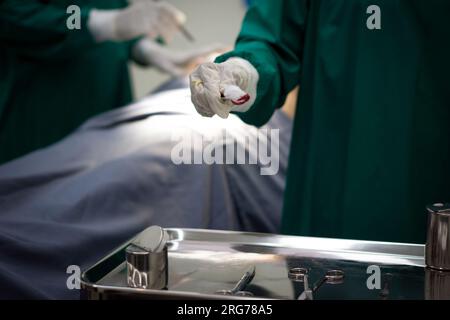 Un moment intense dans une salle d'opération très éclairée où une équipe de chirurgiens focalisée, opère rapidement sur un patient. Banque D'Images