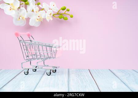 Vide jouet métal supermarché panier sur plancher en bois avec fleur blanche d'orchidée. Banque D'Images