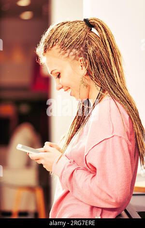 Enveloppée dans son smartphone, une fille avec des tresses en boîte dans un sweat à capuche rose incarne parfaitement le divertissement numérique d'aujourd'hui Banque D'Images