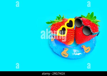Vue de haut en bas de deux fraises, enfilant des lunettes de soleil élégantes, flottant sur un flotteur gonflable dans la piscine. Concept de vacances d'été doux. Banque D'Images