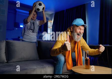 Heureux couple de personnes âgées regardant le soccer à la télévision et célébrant la victoire Banque D'Images