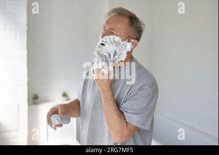 Homme senior rasant le visage appréciant la routine quotidienne dans la salle de bain à la maison Banque D'Images