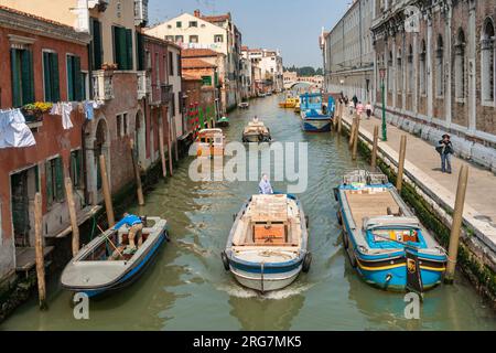 Venise, Italie - 11 avril 2007: Les gens transportent des marchandises sur un navire au canal étroit de venise avec des bateaux de stationnement, Italie. Banque D'Images