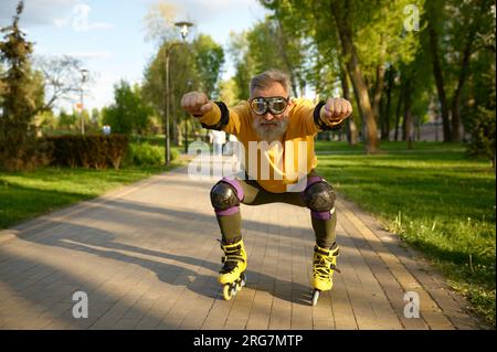 Homme senior portant des lunettes drôles monte sur des patins à roulettes dans le parc Banque D'Images