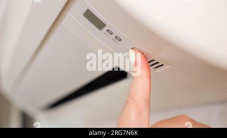 La main de femme appuie sur le bouton pour allumer le climatiseur Banque D'Images