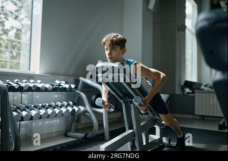 Adolescent garçon engagé dans l'entraînement sportif avec des haltères à la salle de gym Banque D'Images