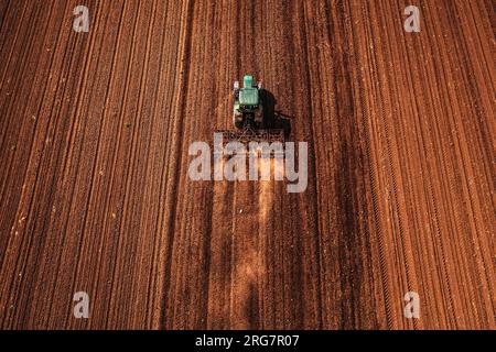 Tracteur agricole avec timon attaché effectuant le travail du sol dans les champs avant la saison de semis, drone de tir aérien pov vue grand angle Banque D'Images