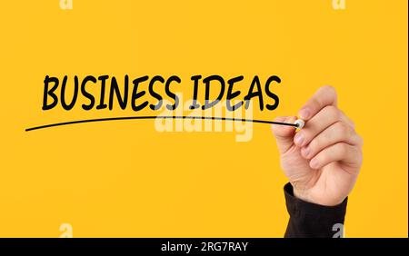 Concept d'idées d'affaires créatives. Main masculine trace une ligne sous le mot idées d'affaires sur fond jaune. Banque D'Images