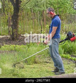 Travailleur tondant de l'herbe haute avec un coupe-herbe électrique ou à essence Banque D'Images