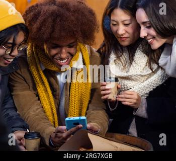 Groupe d'amis multiethniques avec téléphone portable s'amuser tout en buvant du café pendant l'hiver dans une ville Banque D'Images
