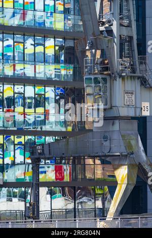 Ancienne grue de cargaison en face de la façade en verre d'un immeuble de bureaux, dans elle est reflétée le Colorium de grande hauteur, façade avec des panneaux de verre colorés, Archi Banque D'Images