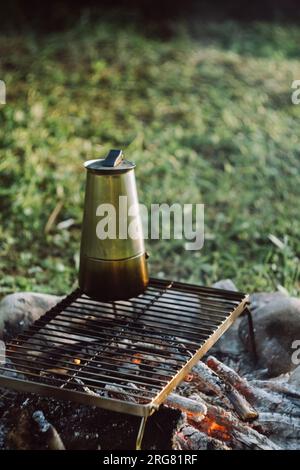 Gros plan de la cafetière geyser sur un feu de joie chaud dans le parc d'été vert au lever ou au coucher du soleil. Vibrations de camping, nature et mode de vie en plein air humeur conc Banque D'Images
