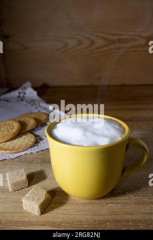 Délicieux café dans une tasse jaune avec des biscuits sur le fond, le tout sur une table en bois.tons chauds en contraste avec le jaune frappant de la tasse Vertica Banque D'Images