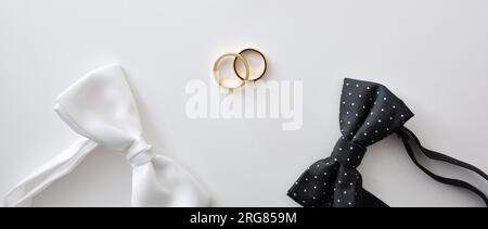 Fond de mariage gay conceptuel avec noeud papillon à pois noir et blanc et anneaux de mariage au milieu. Vue de dessus. Banque D'Images