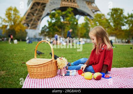 Adorable fille d'enfant d'âge préscolaire ayant pique-nique près de la tour Eiffel à Paris, France. Enfant heureux jouant avec des jouets dans le parc un jour d'automne. Enfant appréciant guérir Banque D'Images