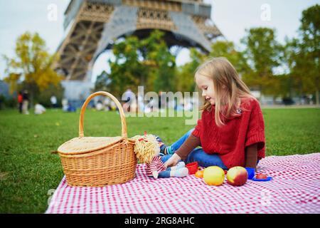 Adorable fille d'enfant d'âge préscolaire ayant pique-nique près de la tour Eiffel à Paris, France. Enfant heureux jouant avec des jouets dans le parc un jour d'automne. Enfant appréciant guérir Banque D'Images