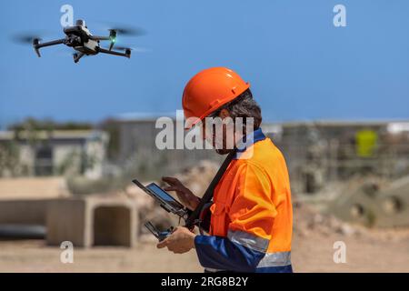 Opérateur de drone avec télécommande pour une caméra UAV thermique, arpentant un chantier, dans une zone industrielle Banque D'Images