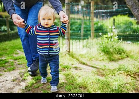 Homme avec une petite fille de 1 ans dans le parc. Père aidant sa fille à faire les premiers pas. Tout-petit apprenant à marcher. Activités familiales avec enfants Banque D'Images