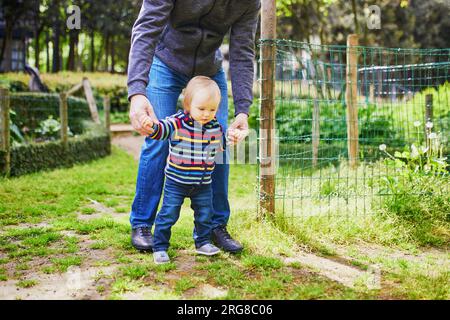 Homme avec une petite fille de 1 ans dans le parc. Père aidant sa fille à faire les premiers pas. Tout-petit apprenant à marcher. Activités familiales avec enfants Banque D'Images