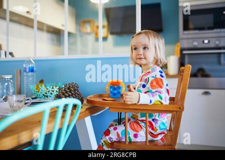 Adorable petite fille en pyjama assis dans une chaise haute tout en prenant le petit déjeuner dans la cuisine à la maison Banque D'Images