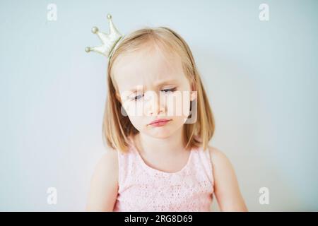 Adorable petite fille en robe rose et couronne dorée habillée en princesse. Portrait d'enfant sur fond clair. Enfant en colère, triste ou sombre Banque D'Images