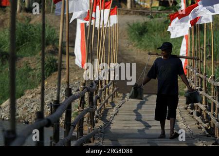 Bantul, Yogyakarta, Indonésie. 8 août 2023. Un homme marche sur un pont de bambou qui divise la rivière Progo à Bantul. Le pont en bambou qui relie les régences de Kulonprogo et de Bantul est décoré de drapeaux rouges et blancs pour accueillir le 78e anniversaire de l'indépendance de la République d'Indonésie le 17 août. (Image de crédit : © Angga Budhiyanto/ZUMA Press Wire) USAGE ÉDITORIAL SEULEMENT! Non destiné à UN USAGE commercial ! Banque D'Images