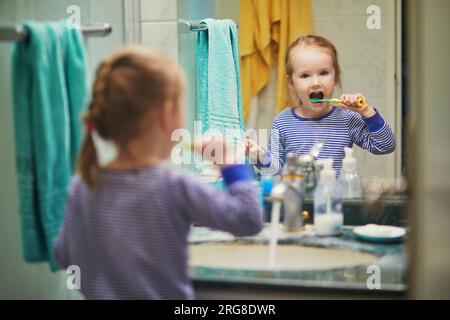 Heureuse petite fille en pyjama se brosser les dents dans la salle de bain le matin ou avant d'aller dormir. Hygiène dentaire pour les petits enfants Banque D'Images