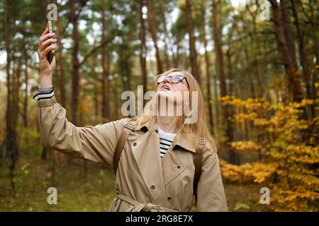 Femme à la recherche de la couverture mobile sur le téléphone mobile se trouve dans une forêt d'automne, pas d'écran de service Banque D'Images