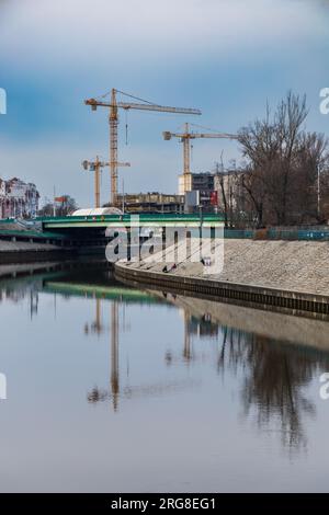 Wroclaw, Pologne - Mars 19 2023 : Grand chantier de construction avec de hautes grues et des cheminées vu de l'autre côté de la rivière Odra dans l'après-midi nuageux Banque D'Images