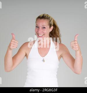 Femme souriante donne le signe Thumbs vers le haut sur fond blanc Banque D'Images