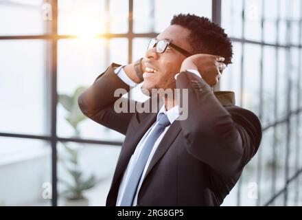 L'homme d'affaires afro-américain dans un élégant costume noir regarde la caméra contre l'arrière-plan de ses collègues Banque D'Images