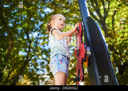 Adorable petite fille sur aire de jeux sur une journée ensoleillée. Enfant d'âge préscolaire jouant à l'extérieur. Activités estivales en plein air pour les enfants Banque D'Images